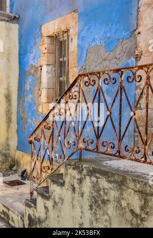 splendido edificio greco in stile elegante e scabro, battuto dal tempo, con pareti dipinte di blu sbiadito e ringhiere arrugginite, dereliche ed edifici intatti. Foto Stock