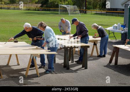 St. Johnsville, Montgomery County, New York: Volontari dipingono stecche di legno durante la riparazione della tribuna al campo di palla comunità. Foto Stock