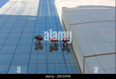 Anonimi pulitori per finestre che puliscono le finestre in altalene o culle all'esterno di un grattacielo cittadino Foto Stock