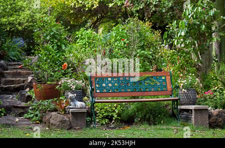 Panca decorativa in ferro battuto e legno circondata da un lussureggiante giardino con fiori e gradini in pietra nelle vicinanze, in Australia Foto Stock