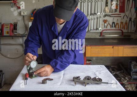 Immagine delle mani di un meccanico nella sua officina che, con uno strumento di precisione spessimetro, misura parti meccaniche. Meccanica di precisione Foto Stock