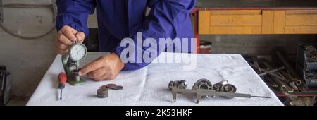 le mani di un meccanico nella sua officina che, con uno strumento di precisione con spessimetro, misura le parti meccaniche. Relativo alla meccanica di precisione. Foto Stock