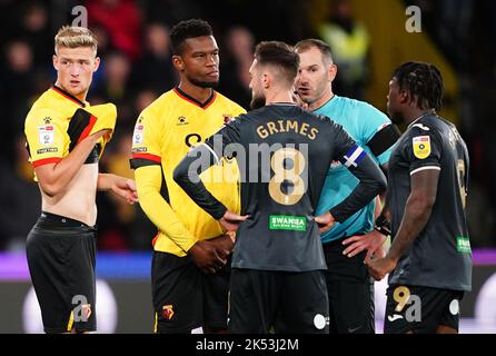 L'arbitro della partita Tim Robinson parla ai giocatori dopo che il gioco si è fermato a causa di problemi con le apparecchiature di comunicazione dei funzionari durante la partita del campionato Sky Bet a Vicarage Road, Watford. Data immagine: Mercoledì 5 ottobre 2022. Foto Stock