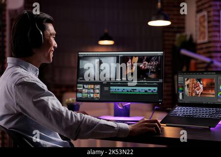 Creator asiatico che modifica filmati con software multimediale, lavorando alla produzione di montaggi su film. Creazione di contenuti video con gradazione del colore ed effetti visivi, utilizzando l'interfaccia del computer a casa. Foto Stock