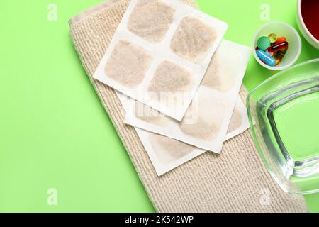 Cerotti di senape con asciugamano, pillole e ciotola d'acqua su fondo verde Foto Stock