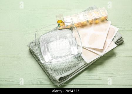 Cerotti di senape con asciugamano, ciotola d'acqua e pillole su fondo di legno verde Foto Stock