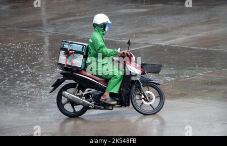 Uomo con una scatola di consegna su un giro in moto sotto la pioggia Foto Stock