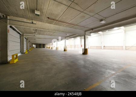 Edificio industriale vuoto con pavimenti in cemento, travi in calcestruzzo prefabbricato, porte scorrevoli in metallo Foto Stock