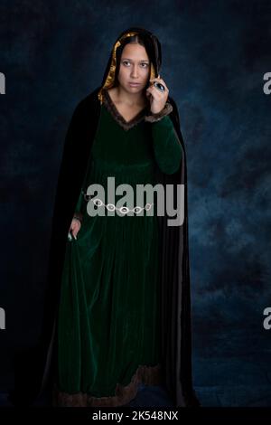 Una donna medievale o fantasy che indossa un vestito di velluto verde e un mantello marrone scuro Foto Stock