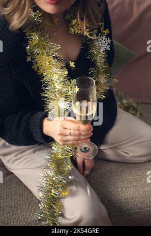 Una donna siede con un bicchiere di champagne nel suo pigiama sul divano. Vista frontale. Foto Stock