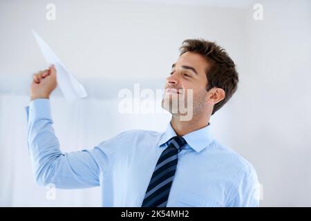 Divertente sul posto di lavoro. Un uomo d'affari sorridente che tiene un aereo di carta e che si prepara a gettarlo nell'aria. Foto Stock