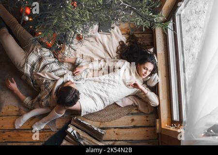 Giovane ragazza coppia amore alla moda, ragazzo sdraiati sulla pelle sul pavimento in accogliente casa di campagna in legno, chalet nella foresta d'inverno. Festeggiamo la vigilia di Capodanno. Regali, famiglia Foto Stock