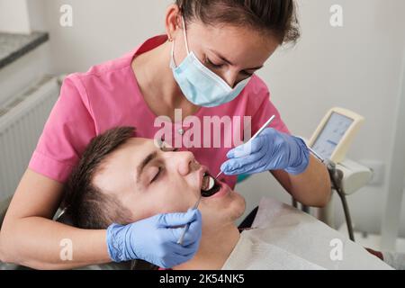 Il dentista esamina la condizione dei denti con l'aiuto dello specchio dentale nei pazienti. Prevenzione della carie. Foto Stock