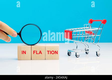 Leva finanziaria ed equilibrio di ricchezza durante il concetto di inflazione. Blocchi di lettere con inflazione parola con una lente d'ingrandimento in mano di donna vicino vuoto s Foto Stock