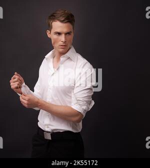 Preparatevi per la palla. Un bel giovane che abbottonava le maniche della camicia su uno sfondo nero. Foto Stock