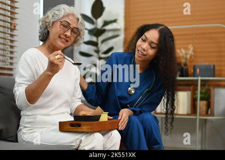 Donna sorridente che si prende cura della cena per le donne anziane. Concetto di servizio sanitario domestico Foto Stock