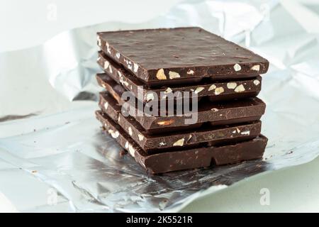 Tavoletta pezzi di cioccolato fondente su una superficie scura e industriale. Fette di cioccolato rotte. Foto Stock