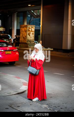 Una signora musulmana tailandese si trova su Sukhumvit Rd, Bangkok, Thailandia utilizzando il suo telefono per scattare una foto. Foto Stock