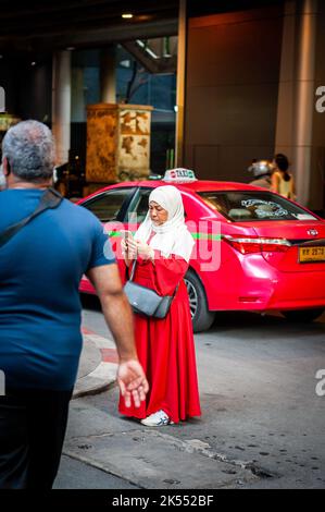 Una signora musulmana tailandese si trova su Sukhumvit Rd, Bangkok, Thailandia utilizzando il suo telefono per scattare una foto. Foto Stock