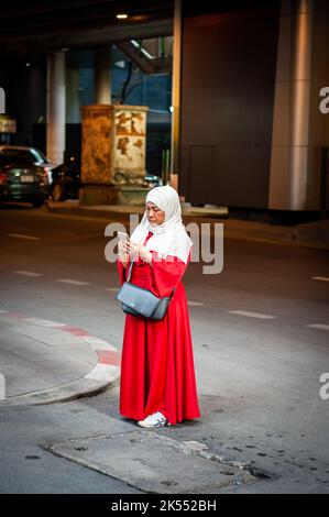 Una signora musulmana tailandese si trova su Sukhumvit Rd, Bangkok, Thailandia utilizzando il suo telefono per scattare una foto. Foto Stock