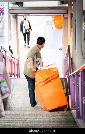 Un uomo thailandese trasporta quello che potrebbe essere un sacchetto per la posta lungo i passi della stazione di Sala Daeng BTS skytrain, Bangkok Thailandia. Foto Stock