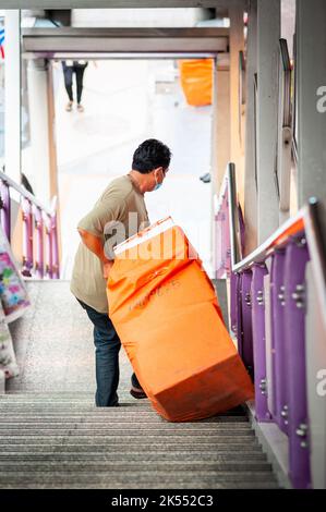 Un uomo thailandese trasporta quello che potrebbe essere un sacchetto per la posta lungo i passi della stazione di Sala Daeng BTS skytrain, Bangkok Thailandia. Foto Stock