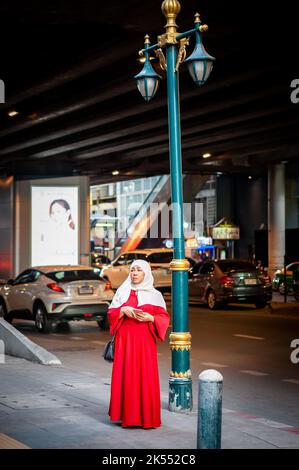 Una signora musulmana tailandese si trova su Sukhumvit Rd, Bangkok, Thailandia utilizzando il suo telefono per scattare una foto. Foto Stock