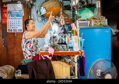 Un marinaio tradizionale lavora fuori alla sua macchina da cucire nella zona di mercato della Comunità di Soi Ruamrudee a Bangkok Thailandia. Foto Stock