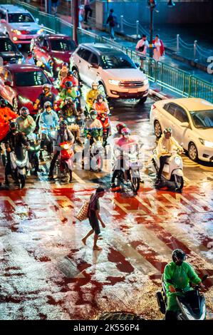 Un uomo tailandese a piedi nudi attraversa la zebra attraversando la famosa e trafficata Asoke montri Rd Incrocio stradale a Bangkok, Thailandia in una serata piovosa bagnata. Foto Stock