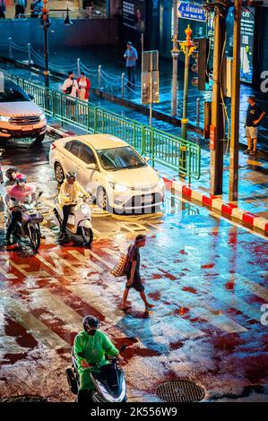 Un uomo tailandese a piedi nudi attraversa la zebra attraversando la famosa e trafficata Asoke montri Rd Incrocio stradale a Bangkok, Thailandia in una serata piovosa bagnata. Foto Stock