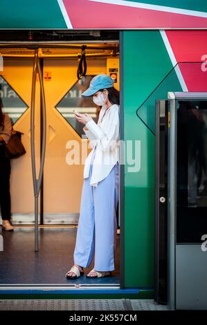 Una giovane ed elegante donna tailandese usa il suo telefono sul treno aereo BTS di Bangkok, Thailandia. Foto Stock