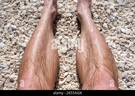 Un mans gambe su una spiaggia di pietra bagnata dopo una nuotata in mare. Foto Stock