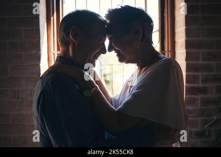 Amore, danza e coppia anziana abbracciano nella finestra del soggiorno, romantico e si legano in casa loro insieme. Romanticismo, pensione e anziani dolci che condividono un Foto Stock