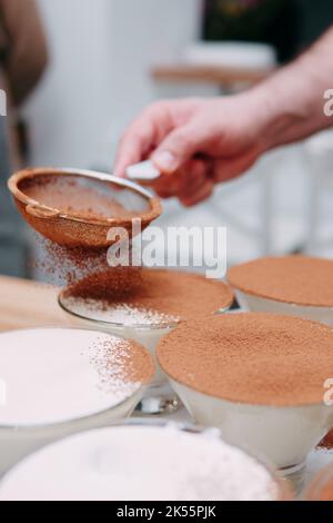 Il processo di preparazione del dessert tiramisù. Il piatto viene cosparso di cacao attraverso un setaccio. Primo piano, messa a fuoco selettiva. Foto Stock