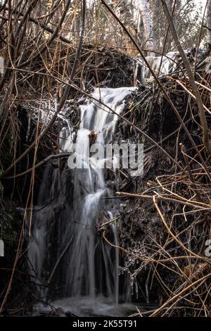 Una lunga esposizione verticale di una piccola cascata che scorre sulle rocce in autunno con erba secca intorno Foto Stock