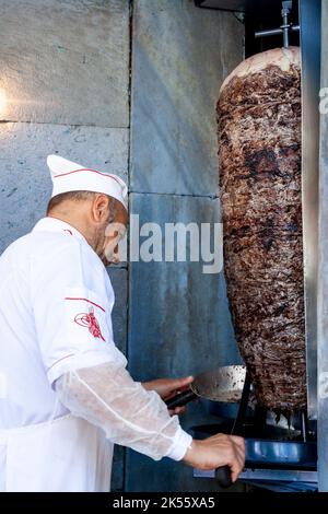 ISTANBUL, TURCHIA - 21 MAGGIO 2022: Sfocatura selettiva su un uomo turco, kebab master chef tagliare uno spiedino di carne per un Doner kebab sandwich a Istanbul, T. Foto Stock