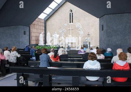 Persone che pregano sulle zampe nel Santuario di Knock, un muro sul quale le apparizioni della Beata Vergine Maria, San Giuseppe, San Giovanni Evangelista, angeli e Gesù apparvero ad un certo numero di bambini nel 1879 Foto Stock