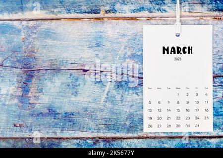 Marzo 2023 pagina del calendario appeso con corda bianca su vecchio sfondo di legno blu. Foto Stock