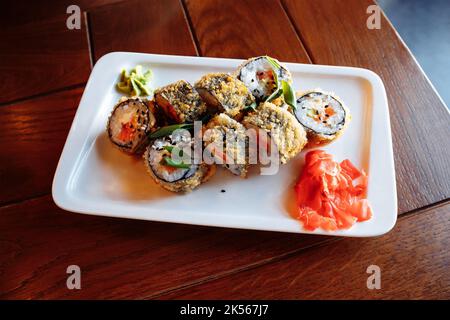 Sushi Maki al forno con tempura, panini al forno su piatto rettangolare bianco. Salmone, avocado, riso, pastella, formaggio cremoso, cipolla verde, nori alghe, sesamo Foto Stock