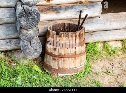 Botte di legno vintage con cerchi in metallo arrugginito vicino casa di legno in estate Foto Stock