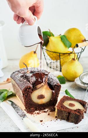 Torta al cioccolato con pere cotte all'interno. Torta di pere al cioccolato o torta di bundt al cioccolato fondente con pera sul tavolo grigio chiaro a casa. Lo chef versa il cioccolato o Foto Stock