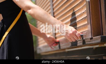 Le mani femminili tengono le maniglie del fermo di legno aprono le tende di legno all'aperto closeup Foto Stock