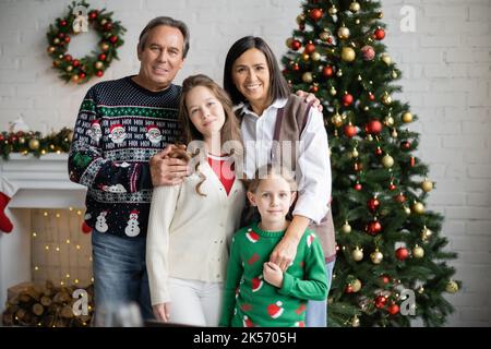 sorrisi guardando la macchina fotografica vicino a felici nonni interracial e albero di natale in soggiorno, immagine di scorta Foto Stock