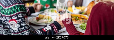 vista parziale del padre anziano e della figlia adulta che tiene le mani e prega vicino a cena sfocata del ringraziamento, banner, immagine di scorta Foto Stock