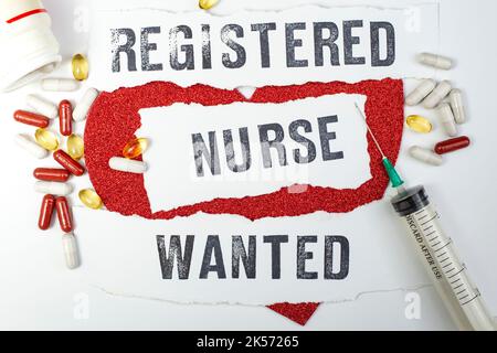 Registered Nurse Wanted scritto con lettere di timbro su carta bianca strappata accanto a siringhe, pillole e un cuore rosso glitter, su sfondo bianco Foto Stock