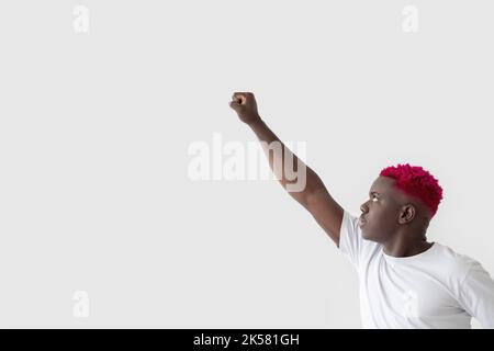 Stile super eroe. Uomo nero coraggioso. Obiettivo impegno. Potenza di forza. Scopo della direzione. Ragazzo africano sicuro con capelli rosa che tiene la mano di pugno su isola Foto Stock