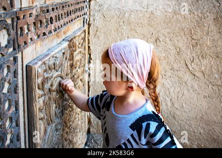 una bambina bussa su una porta scolpita. bella porta di legno vecchio Foto Stock