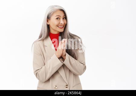 Ritratto di bella donna asiatica di mezza età con capelli grigi, lancette, sorridente e ridente felice, in piedi su sfondo bianco Foto Stock