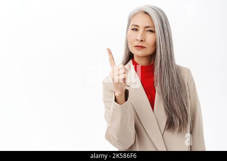 Ritratto di donna asiatica seria di mezza età che guarda severo, tremando il dito e scolding qualcuno, guardando deluso, disapprova smth, in piedi sopra Foto Stock