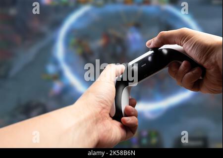 Gamepad moderno, GAM22ICB nelle mani di un giocatore su un background tecnologico. Un giocatore gioca un videogioco su un grande schermo TV. Realtà virtuale, online Foto Stock